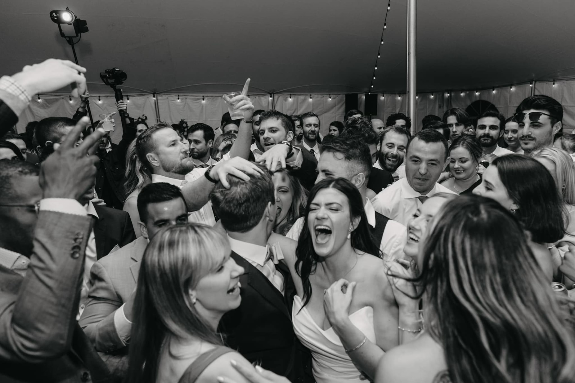A bride and wedding guests celebrating on the dance floor with hands raised